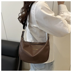 Detailed side view of the brown crescent bag with a wide strap on a model