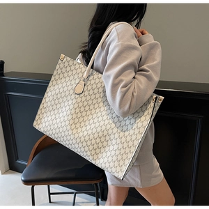 Detail of off-white tote bag with grey M pattern and gold rivets on a model