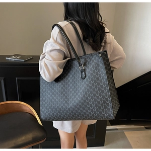 Classic black tote bag with gray M-pattern print and leather straps worn on shoulder