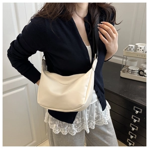 Minimalist beige hobo bag with adjustable wide black strap worn by a model in interior