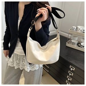 Detail of minimalist cream crescent bag with black adjustable strap and gold text logo