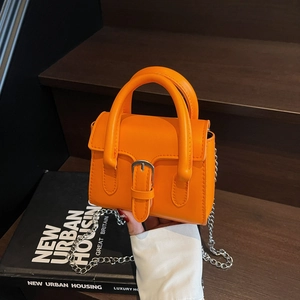 Chic orange mini handbag with silver buckle and chain strap on vintage wooden background