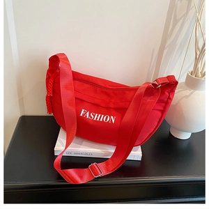 Detail of red crescent shoulder bag with white FASHION print and woven pendant