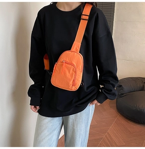 Close-up of orange nylon crossbody chest bag with adjustable black strap on model