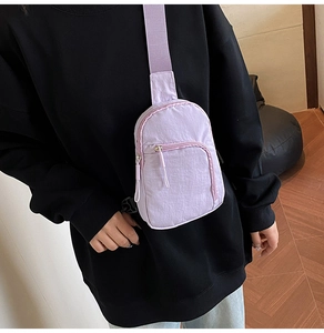 Detail of lavender nylon sling bag with adjustable strap worn over black hoodie