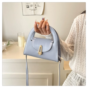 Detail of light blue semi-circle handbag with golden geometric clasp and leather texture