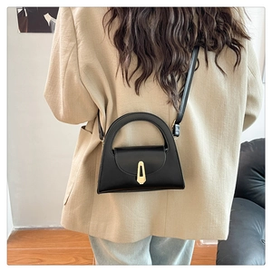 Detailed view of the black crossbody bag with gold metallic clasp on a beige blazer