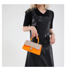 Detail of orange handbag with beige woven texture panel and circular metal turn-lock