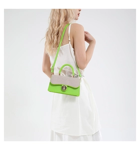 Detail of neon green handbag with beige woven flap and gold twist-lock on white dress