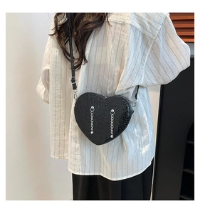 Detail of black heart-shaped crossbody bag with crocodile texture and silver chains