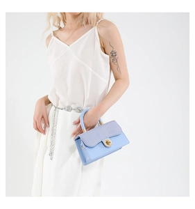 Close-up of light blue handbag with lilac woven flap and golden circular twist lock