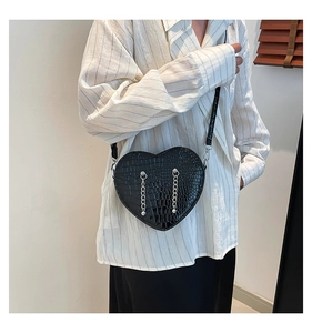 Detail of black heart-shaped crossbody bag with crocodile texture and silver chains