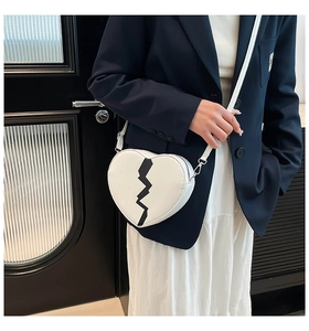 Close-up of white heart-shaped crossbody bag with black lightning bolt detail on blue blazer