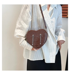 Detail view of heart-shaped crossbody bag with crocodile texture and silver chains
