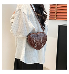 Detail of dark brown heart-shaped crossbody bag with crocodile texture and silver chains