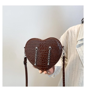 Detail of a brown heart-shaped bag with crocodile texture and silver chain accents