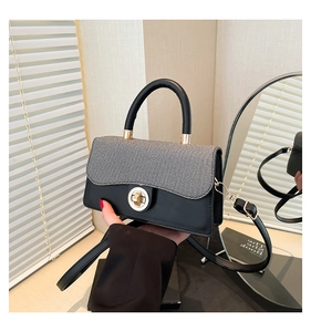 Close-up of woven texture flap and golden lock on gray and black paneled handbag
