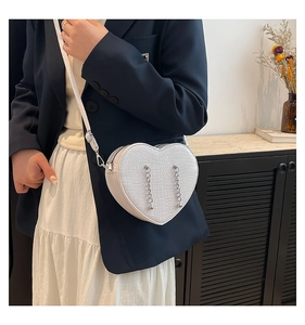 Detailed view of heart-shaped white crossbody bag with crocodile texture and silver chains