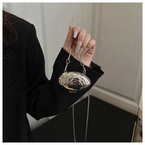 Detail of silver metallic shell bag with mirror finish and slim chain strap on model