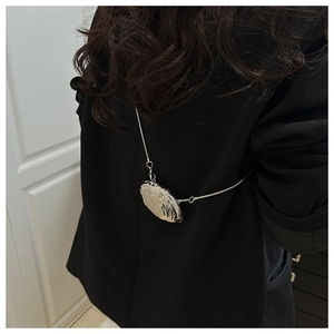 Silver shell-shaped mini metal chain bag accessory shown as a crossbody on black suit