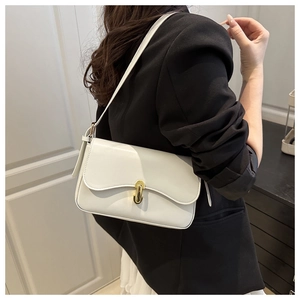 Close-up of a white leather shoulder bag with a gold oval clasp on a black blazer