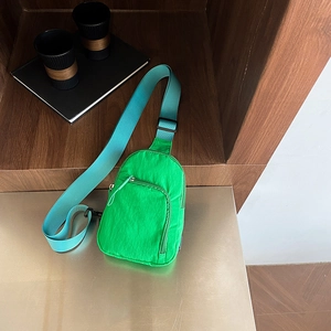 Green nylon chest bag with blue strap and zipper pocket in a modern lifestyle setting