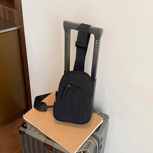 Minimalist black canvas chest bag with adjustable strap displayed on a gray suitcase