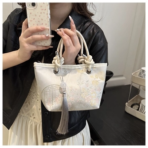 Detailed close-up of floral embroidery on a white satin bucket bag with grey silk tassels