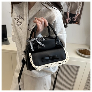 Close-up of black leather handbag with white lace trim, bow, and checkered ribbon detail