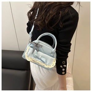 Detail of light blue crossbody bag featuring lace trim, leather bow, and ribbon handle