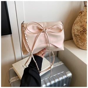 Detailweergave van de roze schoudertas met strik, elegante ketting en getextureerd leer
