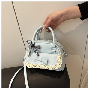 Detail of light blue crossbody bag featuring lace trim and decorative ribbon accents