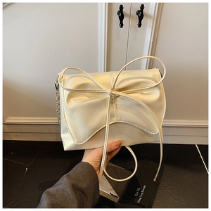 Detail van een crèmewitte PU-lederen crossbodytas met een grote 3D-strik en metalen ketting