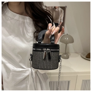 Detail of a mini woven bucket bag with black leather trim and silver metal chain strap