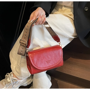 Detail of red leather crossbody bag with ethnic style woven strap on wooden steps
