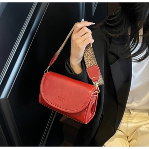 Detail of red leather crossbody bag with ethnic pattern strap and metal clasp detail