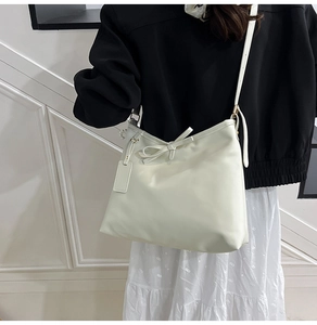 Detail of minimalist cream shoulder bag with bow knot on a model wearing a floral skirt