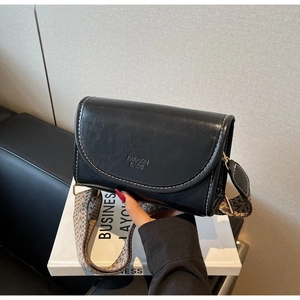 Detail of black leather square bag featuring white contrast stitching and ethnic woven strap