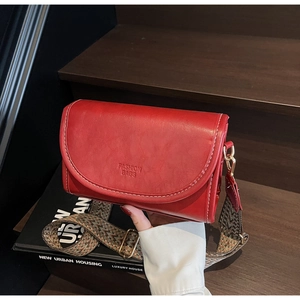 Close-up of red retro crossbody bag featuring white stitching and a woven shoulder strap