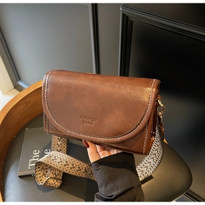 Detail of retro brown leather crossbody bag featuring contrast stitching and woven strap