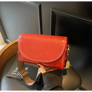 Detail of red leather crossbody bag with white stitching and ethnic jacquard strap