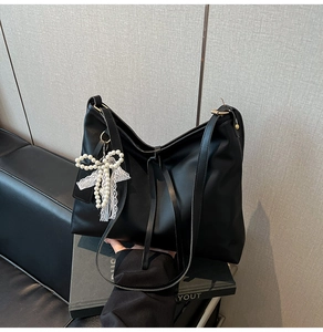 Detail of black leather tote bag with elegant pearl bow and lace charm accessory