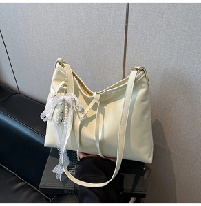 Detail of cream white shoulder bag with lace bow and pearl pendant on smooth leather
