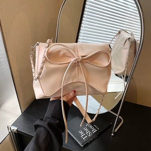 Pink shoulder bag with large bow and silver chain strap shown in front of a mirror