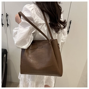 Detail of a dark brown crocodile pattern tote bag shown over the shoulder of a model