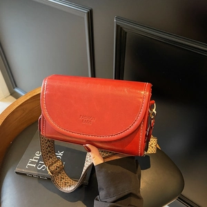 Modern red flap crossbody bag with wide woven strap and white stitching detail
