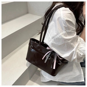 Detail of glossy chocolate brown shoulder bag with decorative ribbons on model