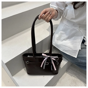 Detailed close-up of dark brown glossy tote bag with decorative ribbons and silver metal rings