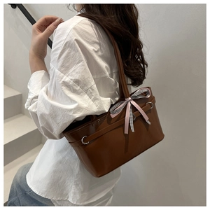 Close-up of brown glossy shoulder bag featuring a pink plaid bow and metal buckle detail
