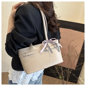Detail of cream shoulder bag with glossy leather and decorative ribbon on model